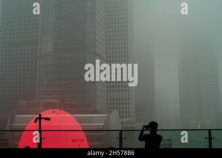 Ein junger Mann fotografiert einen Wolkenkratzer, der in starkem Smog gehüllt ist, im Geschäftszentrum von Peking, China. 06-Nov-2021 Stockfoto
