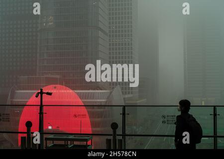 Ein junger Mann fotografiert einen Wolkenkratzer, der in starkem Smog gehüllt ist, im Geschäftszentrum von Peking, China. 06-Nov-2021 Stockfoto