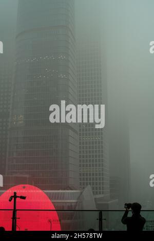 Ein junger Mann fotografiert einen Wolkenkratzer, der in starkem Smog gehüllt ist, im Geschäftszentrum von Peking, China. 06-Nov-2021 Stockfoto
