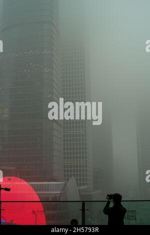 Ein junger Mann fotografiert einen Wolkenkratzer, der in starkem Smog gehüllt ist, im Geschäftszentrum von Peking, China. 06-Nov-2021 Stockfoto