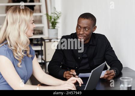 Porträt von zwei Geschäftspartnern, die während der Besprechung in einem minimalen Büro mit einem Laptop arbeiten und Platz für Kopien haben Stockfoto