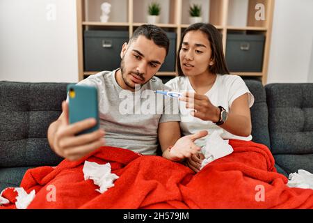 Junges lateinamerikanisches krankes Paar, das zu Hause eine medizinische Fernsultation mit dem Smartphone hat. Stockfoto