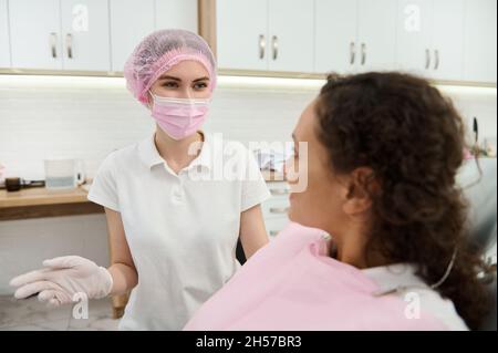 Pretty Zahnarzthelfer, Zahnarzt Hygienist in der schützenden Sicherheit medizinische Kleidung Beratung weibliche Patientin, Kunde der Zahnklinik, geben medizinische rec Stockfoto