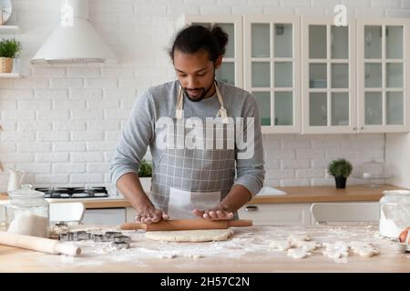 Fokussierter junger afroamerikanischer Mann, der in der heimischen Küche Kekse backt Stockfoto