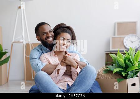 Zufriedene glückliche tausendjährige afroamerikanische liebevolle Familie, Ehemann und Ehefrau umarmen, entspannen in neue Wohnung Stockfoto