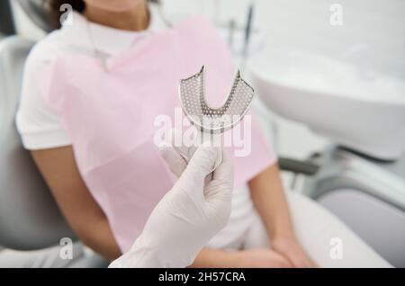 Nahaufnahme der Hand eines Zahnarztes mit Zahnform Zahnärzte Zähne Keramikplatte auf dem Hintergrund eines Patienten auf dem Stuhl des Zahnarztes in Mo gegossen Stockfoto