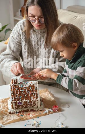 Kleiner Junge mit Mutter, die Weihnachten Lebkuchenhaus zusammen dekoriert, Familienaktivitäten und Traditionen an Weihnachten und Silvester Stockfoto