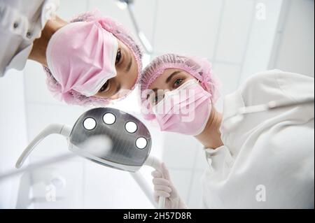 Ansicht von unten der Ärztin Zahnarzt und Zahnarzthelferin Einstellung medizinische Lampe, Instrumente halten und sich zu einem Patienten für medizinische e Stockfoto