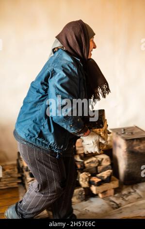 Die alte Frau nimmt den Ziegel mit dem Ruß aus dem Haus heraus, den Abbau des alten Ofens. Neu Stockfoto