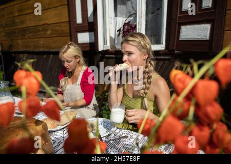 Schwiegertochter isst und beißt in einen Brotaufstrich mit Weißkäse. Frühstück auf dem Land. Stockfoto