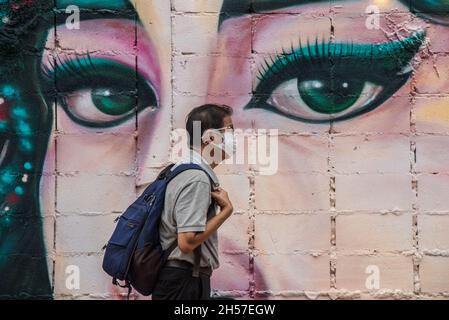 Bangkok, Thailand. November 2021. Ein Mann mit Gesichtsmaske als vorbeugende Maßnahme gegen die Ausbreitung von covid-19 geht an einem Straßenkunstgemälde an der Wand des Khlong Ong Ang Canal vorbei. Kredit: SOPA Images Limited/Alamy Live Nachrichten Stockfoto