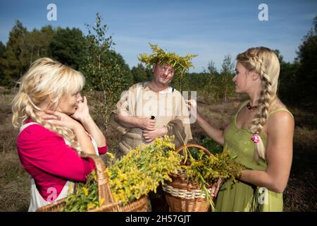 Zwei Kräuterkundige, die auf einer Feldwiese standen, trafen auf einen Mann mit einer Girlande auf dem Kopf. Feldkräuter von Goldrute. Stockfoto