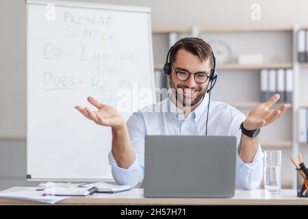 Fröhlich mittleren Alters gutaussehende europäischen männlichen Lehrer in Brille Gesten, schaut auf Laptop-Webcam im Home Office Stockfoto