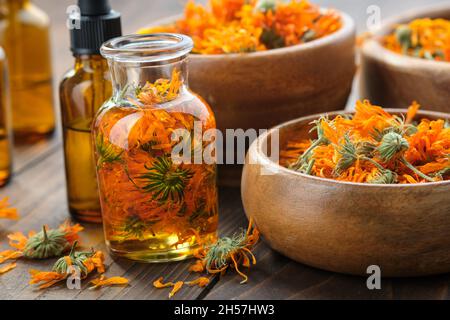 Flaschen mit ätherischem Calendula-Öl oder Infusion, Holzschüsseln und Mörser aus getrockneten gesunden Ringelblumen. Alternative Kräutermedizin. Aum Stockfoto