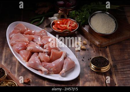 Rohes Huhn biriyani geschnitten ohne Haut auf weißem Tischgeschirr mit Zutaten im Hintergrund mit rustikalem Holzhintergrund platziert angeordnet. Stockfoto