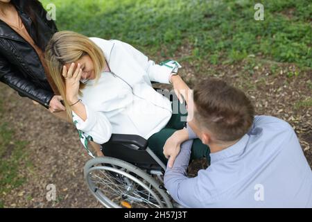 Junge behinderte Frau im Rollstuhl weint in der Nähe eines Mannes, der vor ihr im Park sitzt Stockfoto