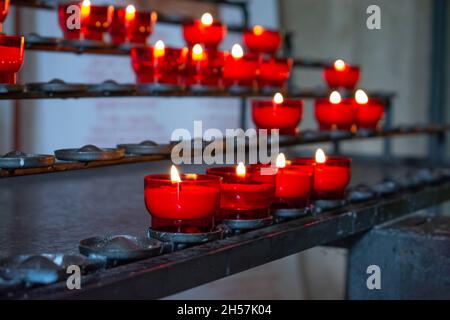 Brennende rote Gebetskerzen in einer katholischen Kirche auf einem Kerzenständer. Selektiver Fokus. Stockfoto