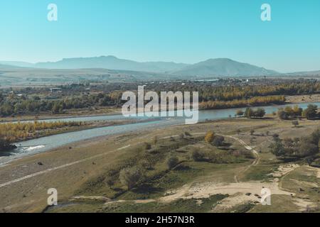 Blick auf den Fluss Mtkvari oder den Fluss Kura von der Felshöhle Uplistsikhe in Georgien, Asien. Flussufer mit Herbstbäumen und Hügeln im Hintergrund Stockfoto