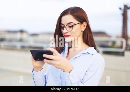 Junge Rotschopf clevere kaukasische Geschäftsfrau Messaging auf dem Smartphone im Freien Stockfoto