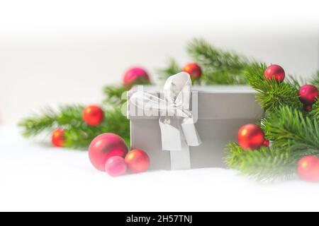 Geschenkbox zu Weihnachten. Rote Weihnachtskugel-Ornamente und Tannenzweige oder Kiefernzweige. Stockfoto