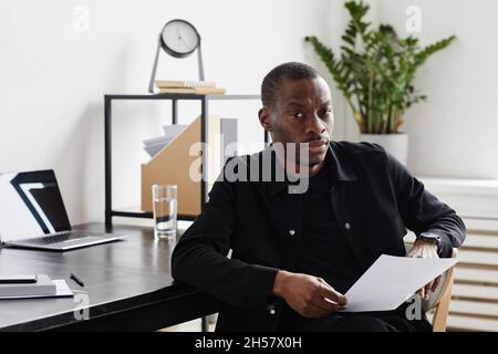 Porträt eines ernsthaften afroamerikanischen Geschäftsmannes, der beim Sitzen am Schreibtisch im Heimbüro auf die Kamera schaut, Kopierfläche Stockfoto