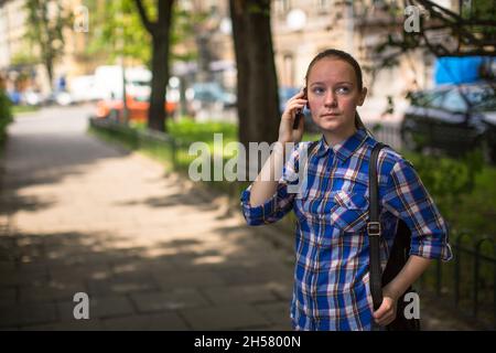 Ein Teenager-Mädchen, das in einem Sommerpark mit ihrem Handy spricht. Stockfoto