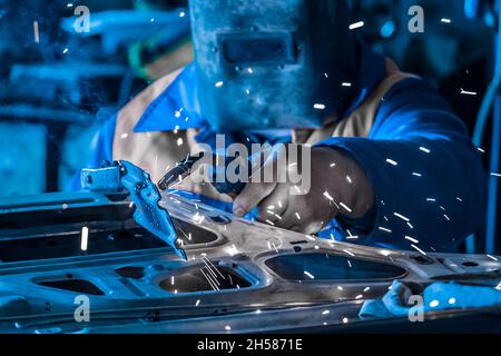 Der Prozess des Schweißens von Funken während der Reparatur einer Autotür in der Werkstatt eines Industriewerks. Stockfoto