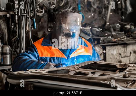 Der Schweißer im Schutzschild beschäftigt sich mit den Schweißarbeiten und der Reparatur der Autotür in der Werkstatt des Industrieunternehmens. Stockfoto