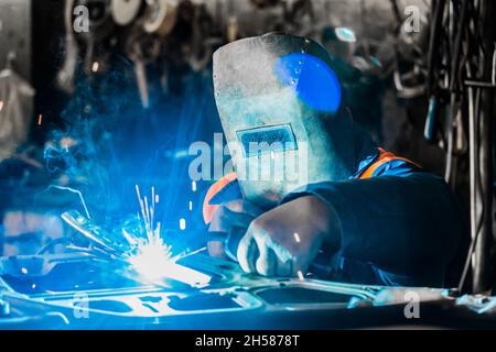 Schweißer Mann in einer Schutzmaske aus Eisen ist in den Prozess der Schweiß-und Metallarbeiten in der Werkstatt eines Industriewerks beschäftigt. Stockfoto