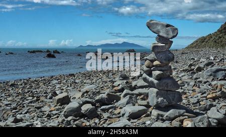 Ein Felsblock auf dem Kapiti Coast Beach Track zwischen Pukerua Bay und Plimmertion. Kapiti Island vor der Küste Stockfoto