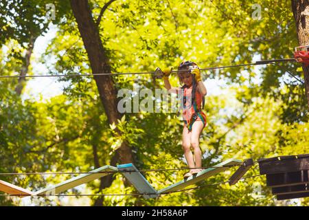 Das konzentrierte Mädchen überwindet sorgfältig Hindernisse im Seilpark Stockfoto