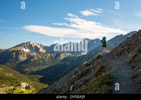 Wanderfrau mit Wanderstöcken an einem sonnigen Tag auf einem steilen Weg in schroffem Berggelände im Sommer, Indian Peaks Wilderness Area, Colorado, USA Stockfoto