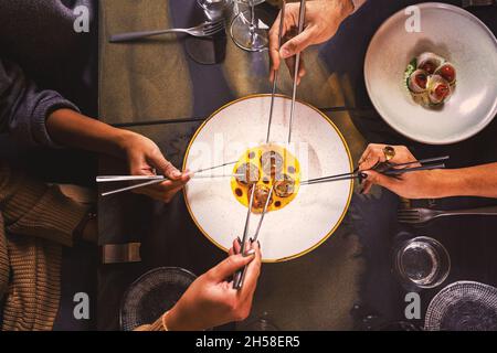 Orientalisches Gericht auf der Basis von Jakobsmuscheln – Nahaufnahme der Tischplatte mit Händen, die eine Portion Essen mit chinesischen Essstäbchen nehmen Stockfoto