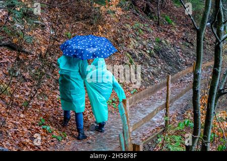 Frau mit Kindern auf Regenmänteln, die auf einem eisbedeckten Weg um den von Eis bedeckten See Synevyr, die Karpaten, Ukraine, wandern Stockfoto