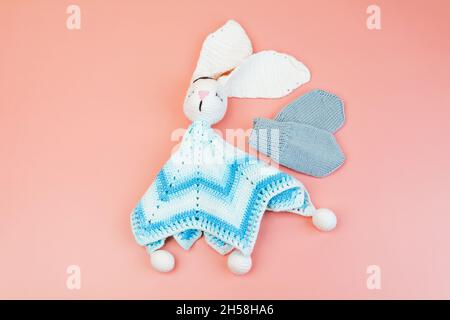 Handgefertigtes, gestricktes blaues und weißes Häschen-Spielzeug und graue Fäustlinge für Frühgeborene für Frühgeborene, isoliert auf rosa Hintergrund Stockfoto