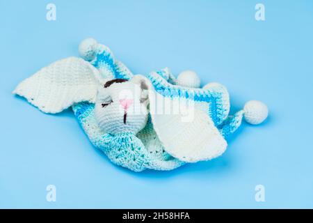 Handgemachte gestrickte blaue und weiße Hase aus Stofffasern für Babys auf blauem Hintergrund isoliert. Stockfoto