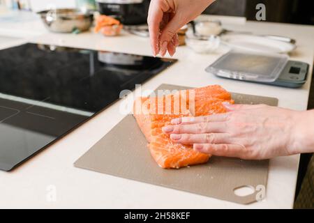 Frau salzt rotes Fischfilet. Nahaufnahme der Zubereitung leicht gesalzener roter Fische. Stockfoto