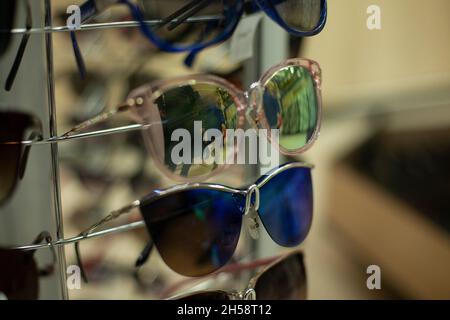 Viele Gläser im Laden. Sonnenbrillen im Angebot. Stellen Sie sich mit einer Brille auf, um die Augen vor Sonnenlicht zu schützen. Stockfoto