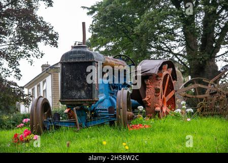 Vintage Fordson Traktor steht auf Gras auf einer Wiese mit Blumen um ihn herum Stockfoto