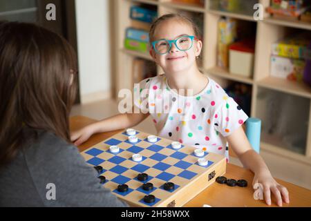 Mädchen mit Down-Syndrom spielt mit ihrer Schwester in Quarantäne Checkers Stockfoto