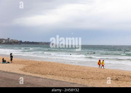 Surfrescue Freiwillige Rettungsschwimmer, die an einem bewölkten grauen Himmel am Ufer des Manly Beach in Sydney spazieren gehen, Sydney, Australien Stockfoto