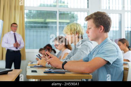 Jugendliche Schüler, die während des Unterrichts Smartphones benutzen Stockfoto