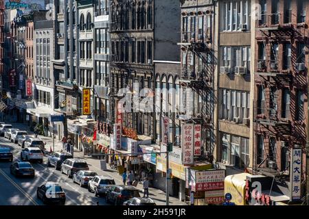 East Broadway, Chinatown, New York City, USA. 26. September 2021. Geschäftige Haupteinkaufsstraße in chinatown. Wohngebäude mit Geschäften auf Zaun Stockfoto