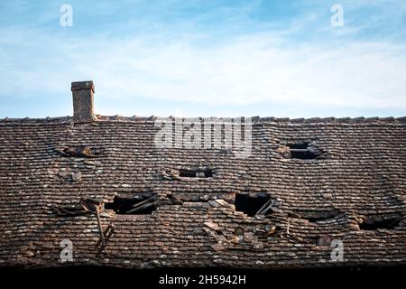 Bild eines alten Daches, das dringend repariert werden muss, hauptsächlich in schlechtem Zustand, mit beschädigten Fliesen und fehlenden Schindeln und riesigen Löchern. Stockfoto