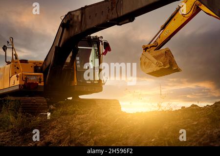 Baggerlader auf der Baustelle graben Boden mit Eimer Baggerlader. Bulldozer am Abendhimmel. Bagger auf der Baustelle geparkt. Maschine mit Erdbewegung. Stockfoto