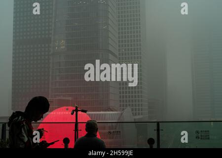 Ein junger Mann raucht, während ein anderer die Wolkenkratzer im chinesischen CBD in starkem Smog sieht. 06-Nov-2021 Stockfoto