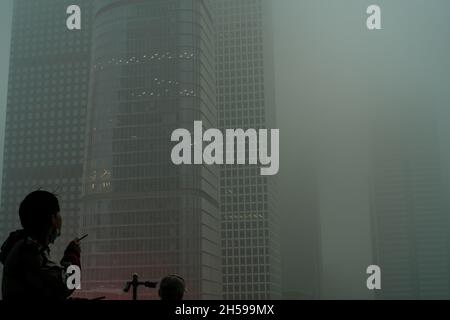 Ein junger Mann schaut auf die Wolkenkratzer, die in starkem Smog im chinesischen CBD von Peking gehüllt sind. 06-Nov-2021 Stockfoto