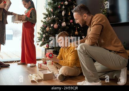 Lächelnder bärtiger Vater, der die Schulter des Sohnes berührte, der einen neuen bluetooth-Lautsprecher ansah, bescherte ihm Weihnachten Stockfoto