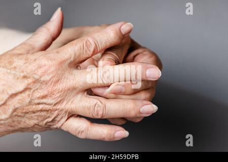 Eine ältere Frau massiert ihre Finger und hat Schmerzen in den Gelenken. Grauer Hintergrund, Nahaufnahme der Hände. Das Konzept von Rheuma und Arthritis. Stockfoto