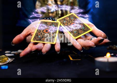 Kartomantie. Die Wahrsagerin hält zwei Tarot-Karten auf ihren Handflächen aus. Der Tierkreiskreis wird über der Hand mit den Karten dargestellt. Das Konzept von div Stockfoto